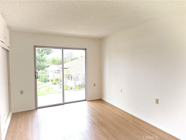 spare room with baseboards, light wood-type flooring, and a textured ceiling