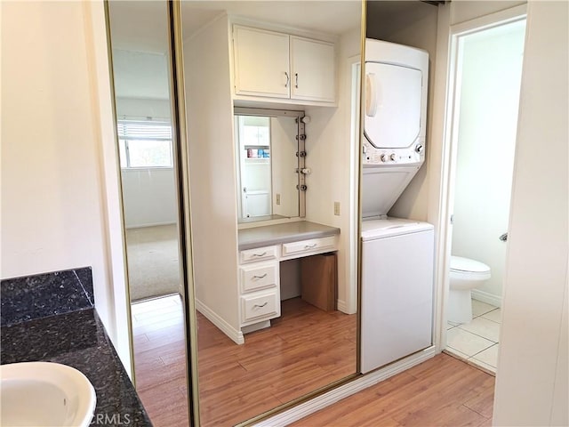 laundry room featuring a sink, laundry area, stacked washing maching and dryer, and light wood-style flooring