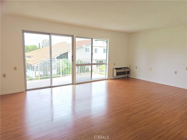 spare room with baseboards, a textured ceiling, heating unit, and wood finished floors