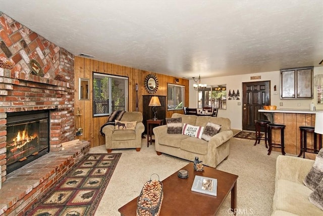 carpeted living room with visible vents, an inviting chandelier, wooden walls, and a brick fireplace