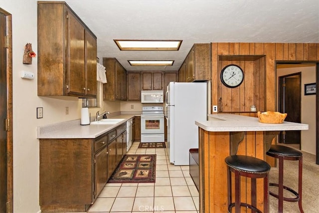 kitchen with a sink, a breakfast bar, light countertops, white appliances, and a peninsula