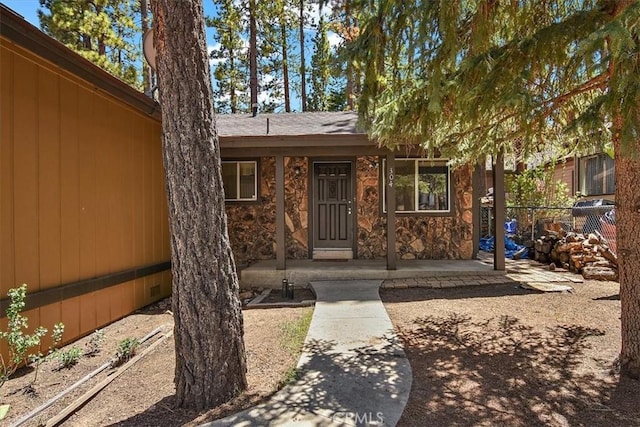 entrance to property featuring stone siding and fence