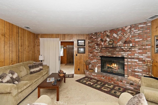 living area featuring a brick fireplace, visible vents, wood walls, and carpet