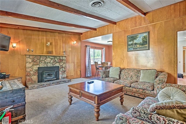 carpeted living area featuring beam ceiling, a wood stove, visible vents, and wooden walls