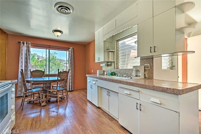 kitchen featuring decorative backsplash, light wood finished floors, a sink, visible vents, and tile countertops