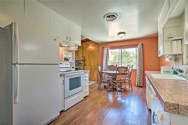 kitchen featuring white appliances, under cabinet range hood, dark wood-style flooring, a sink, and visible vents