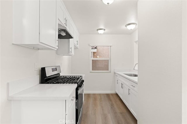 kitchen with light wood-style floors, under cabinet range hood, light countertops, a sink, and stainless steel gas range