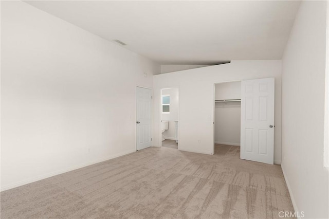 unfurnished bedroom featuring light colored carpet, a closet, vaulted ceiling, a walk in closet, and visible vents