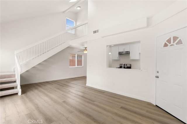 unfurnished living room with visible vents, stairway, wood finished floors, and high vaulted ceiling