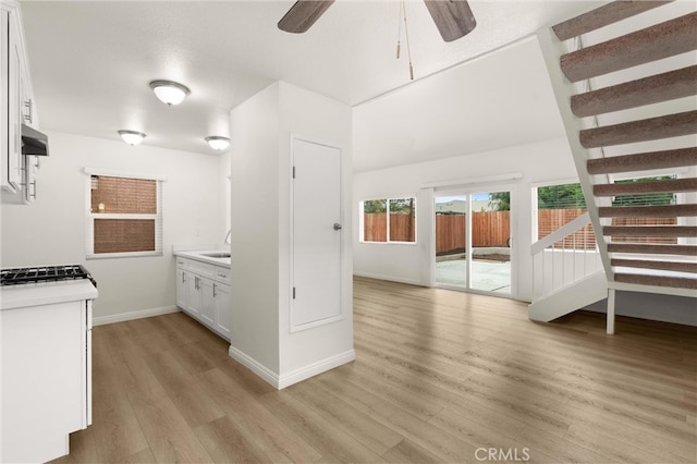 kitchen featuring baseboards, light countertops, light wood finished floors, white cabinetry, and a ceiling fan