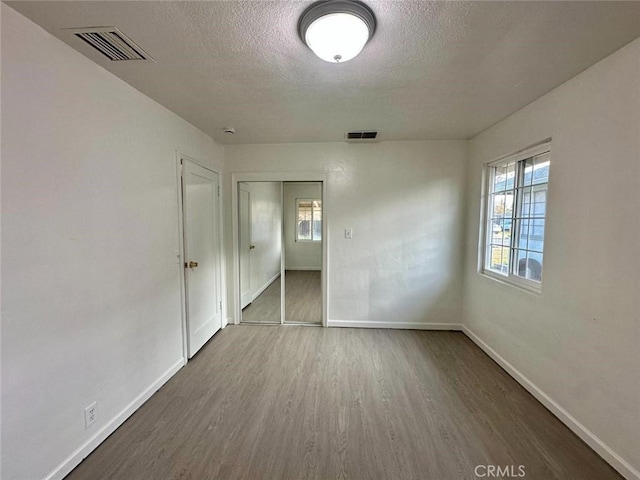 empty room with wood finished floors, visible vents, baseboards, and a textured ceiling