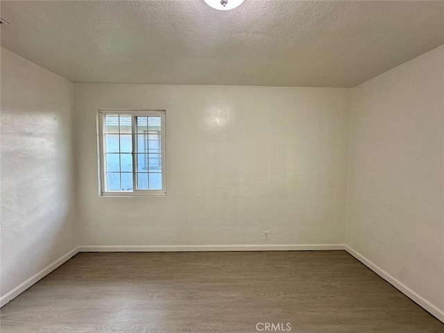 unfurnished room with a textured ceiling, wood finished floors, and baseboards