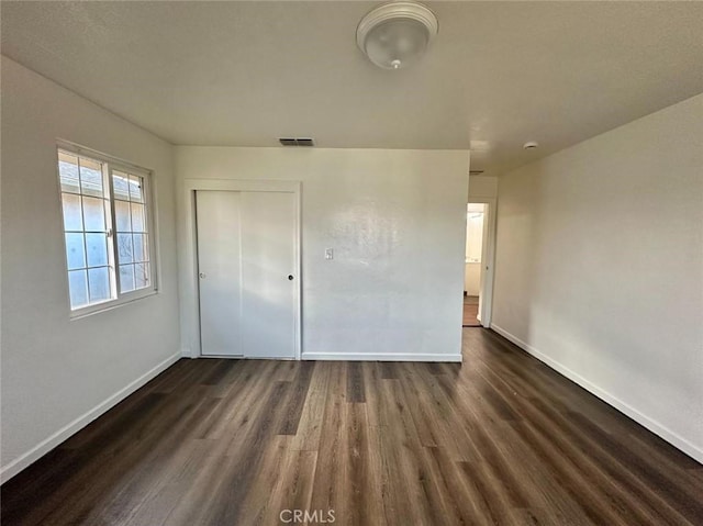unfurnished bedroom with visible vents, a closet, dark wood-style floors, and baseboards