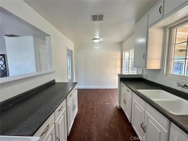 kitchen featuring dark wood-style floors, a sink, a healthy amount of sunlight, visible vents, and dark countertops
