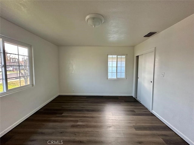 unfurnished bedroom featuring visible vents, dark wood-style flooring, a closet, and baseboards