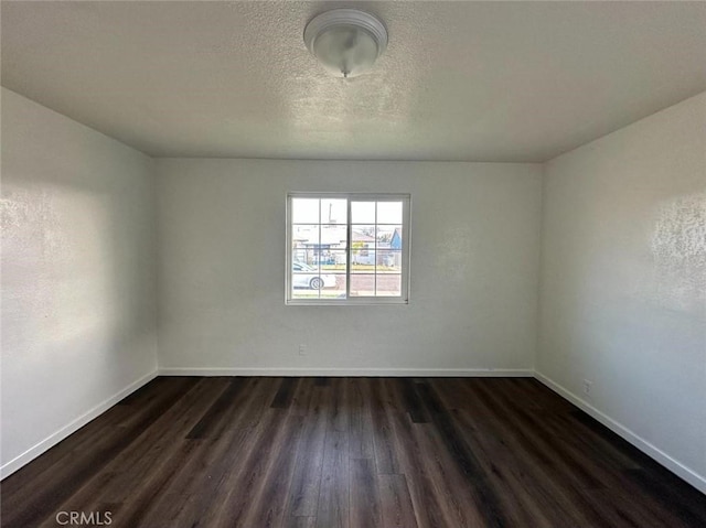 unfurnished room featuring dark wood-type flooring, a textured ceiling, and baseboards