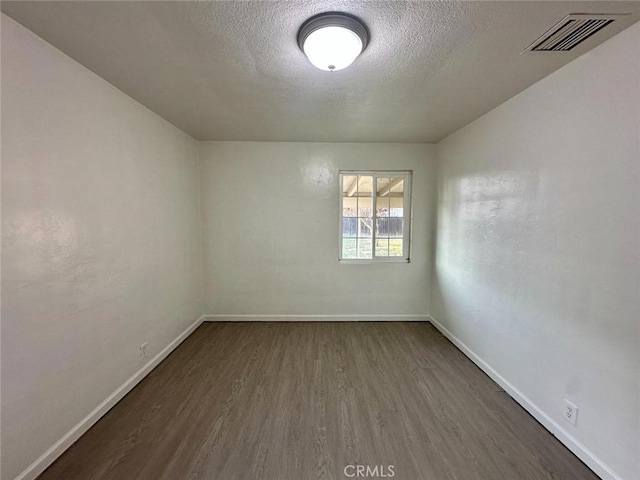 unfurnished room featuring dark wood finished floors, visible vents, a textured ceiling, and baseboards