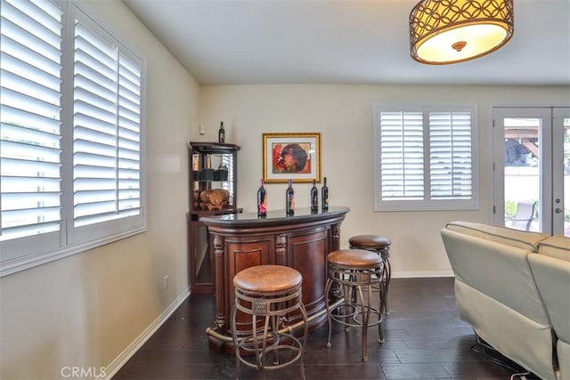 bar featuring dark wood-style floors, a bar, a wealth of natural light, and baseboards