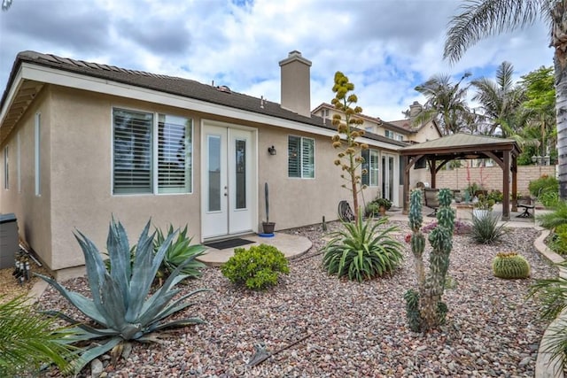 rear view of property featuring a chimney, a gazebo, a patio area, stucco siding, and french doors