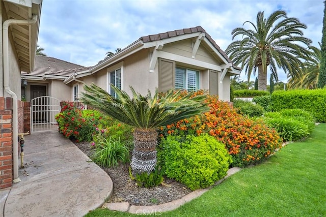 view of property exterior featuring stucco siding, a tile roof, and a lawn