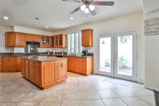 kitchen featuring brown cabinets, glass insert cabinets, a sink, under cabinet range hood, and french doors