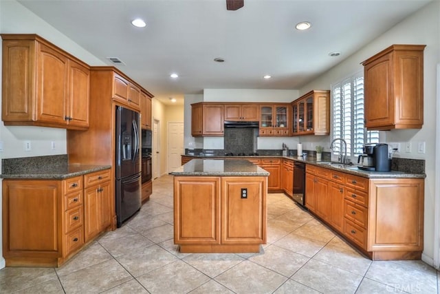 kitchen with glass insert cabinets, brown cabinetry, a kitchen island, black appliances, and a sink