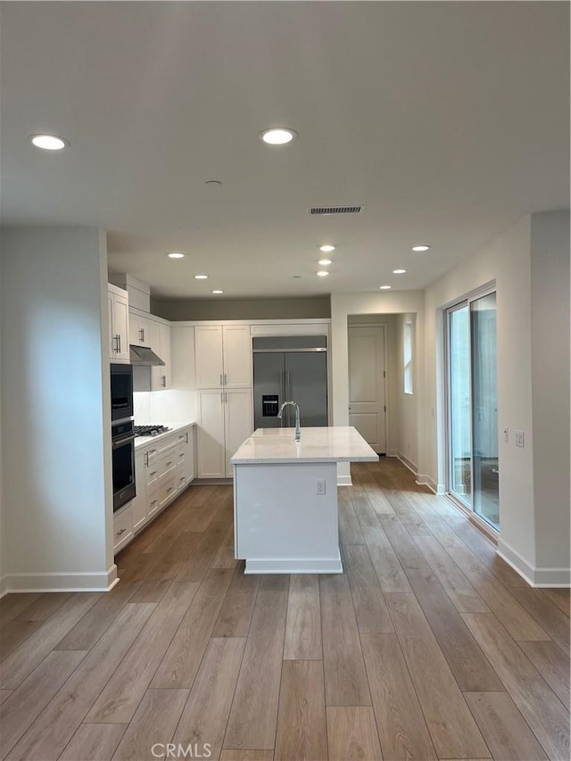 kitchen featuring under cabinet range hood, built in appliances, visible vents, white cabinets, and wood finished floors