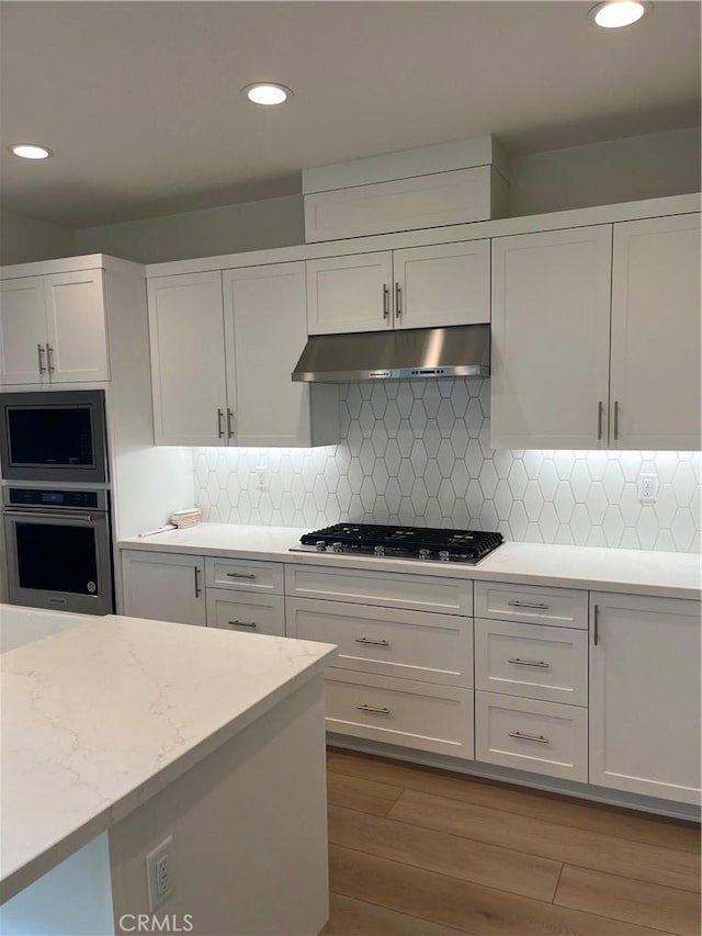 kitchen with recessed lighting, stainless steel appliances, under cabinet range hood, white cabinetry, and wood finished floors