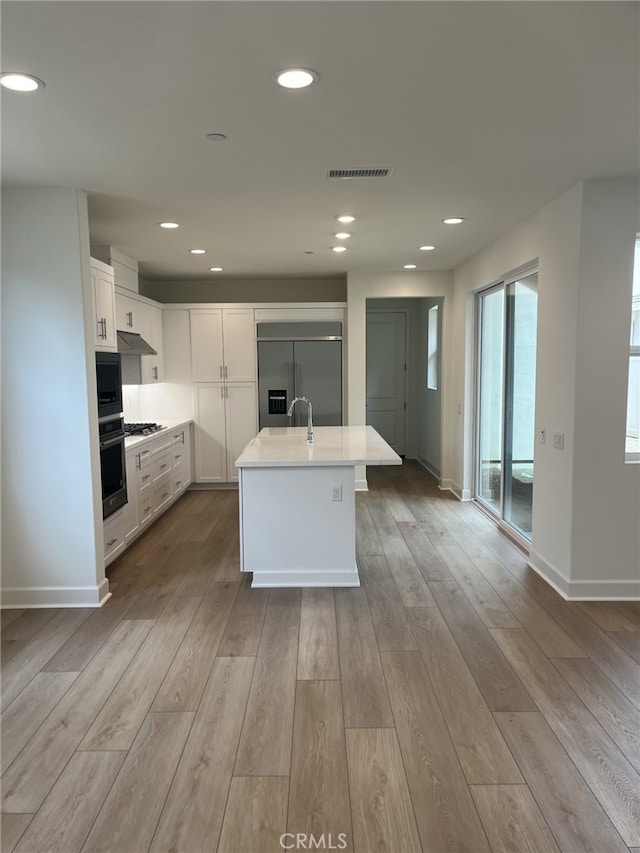 kitchen with under cabinet range hood, built in refrigerator, visible vents, white cabinetry, and light countertops