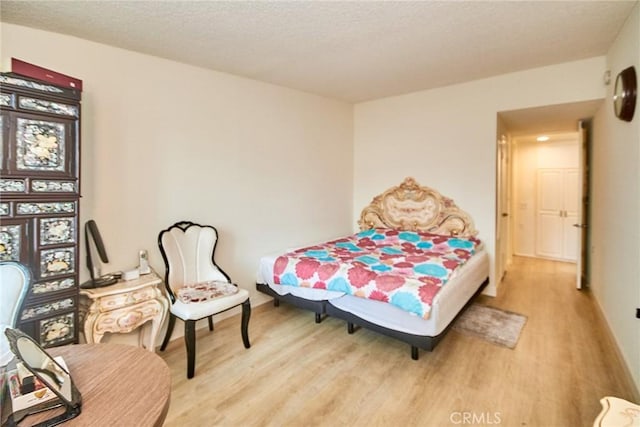 bedroom featuring baseboards, a textured ceiling, and light wood-style flooring