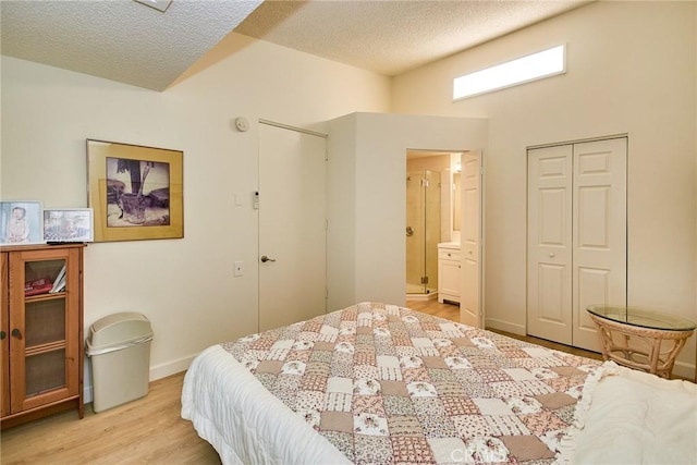 bedroom with light wood finished floors, a textured ceiling, baseboards, ensuite bathroom, and a closet