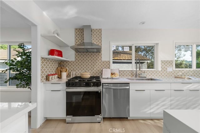 kitchen with modern cabinets, wall chimney range hood, range with gas cooktop, a sink, and dishwasher