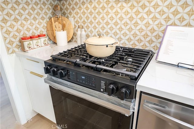 kitchen featuring stainless steel range with gas stovetop, light countertops, white cabinetry, and backsplash