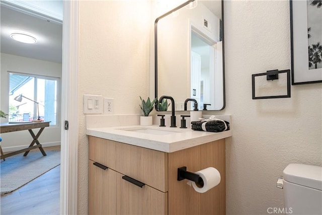 half bath featuring vanity, baseboards, wood finished floors, and toilet