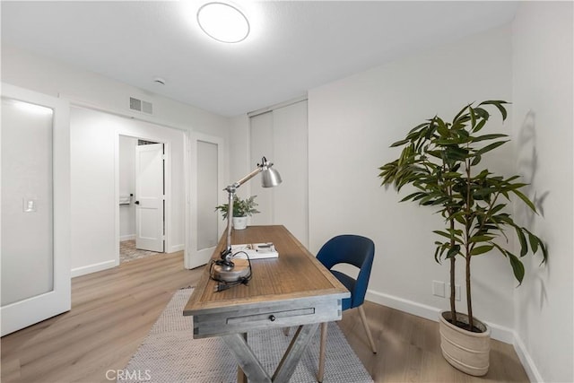 office space with light wood-style floors, baseboards, and visible vents