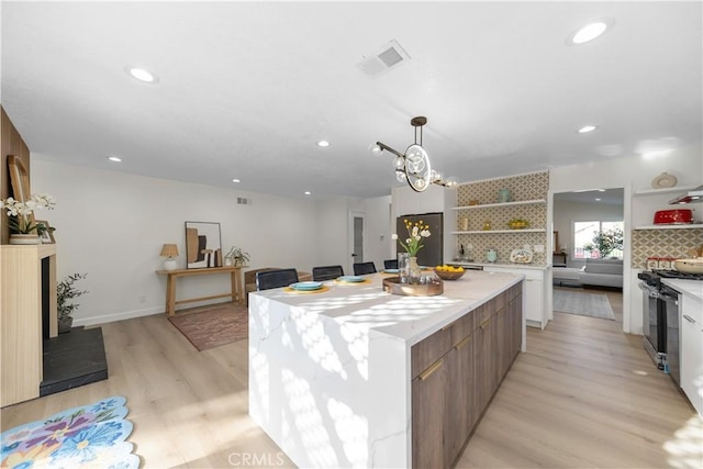 kitchen featuring visible vents, gas range, a center island, open shelves, and light wood-style floors