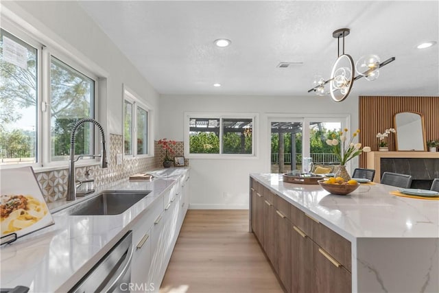 kitchen featuring light stone countertops, dishwasher, a sink, light wood finished floors, and recessed lighting