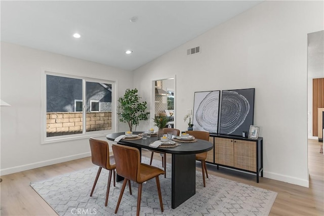 dining space featuring light wood-style floors, baseboards, lofted ceiling, and visible vents