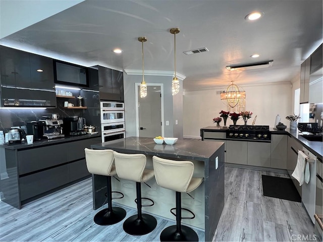 kitchen with dark countertops, light wood finished floors, a kitchen breakfast bar, multiple ovens, and modern cabinets