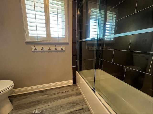 bathroom featuring baseboards, combined bath / shower with glass door, wood finished floors, and toilet