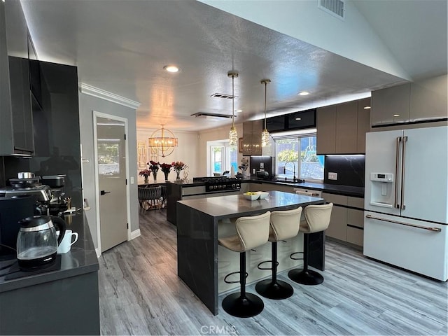 kitchen with dark countertops, high end white fridge, a sink, light wood-style floors, and visible vents