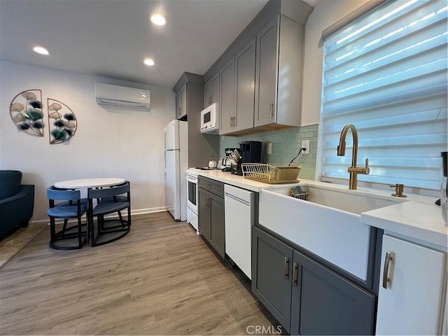 kitchen featuring white appliances, light countertops, a wall unit AC, a sink, and light wood-style flooring