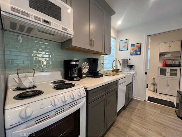kitchen featuring white appliances, light countertops, tasteful backsplash, a sink, and gray cabinetry
