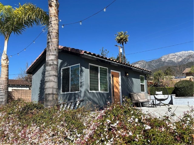 view of home's exterior featuring fence, a patio, stucco siding, a tiled roof, and a mountain view