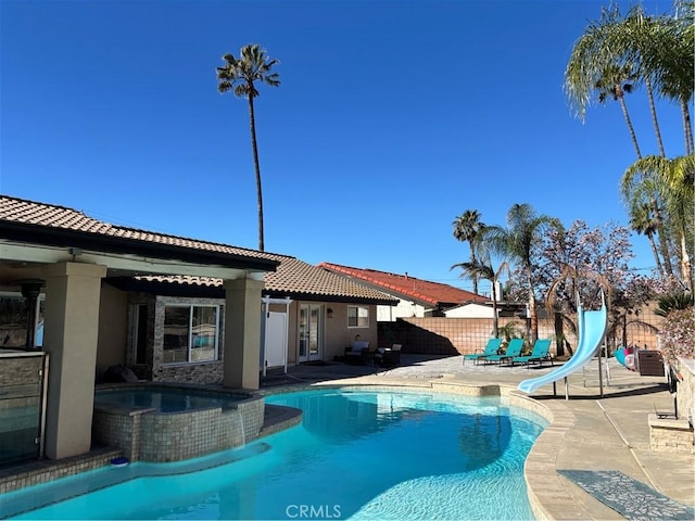 view of pool featuring a patio, a fenced backyard, a water slide, and a pool with connected hot tub