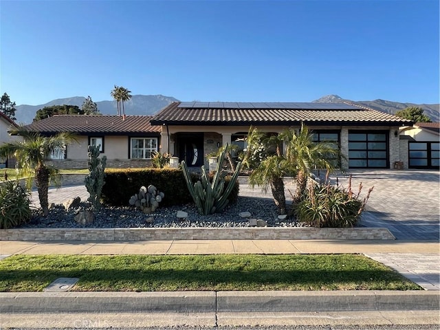 view of front facade with a garage, roof mounted solar panels, a mountain view, decorative driveway, and a tiled roof
