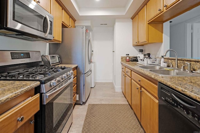 kitchen with stainless steel appliances, a sink, baseboards, light wood-type flooring, and a tray ceiling