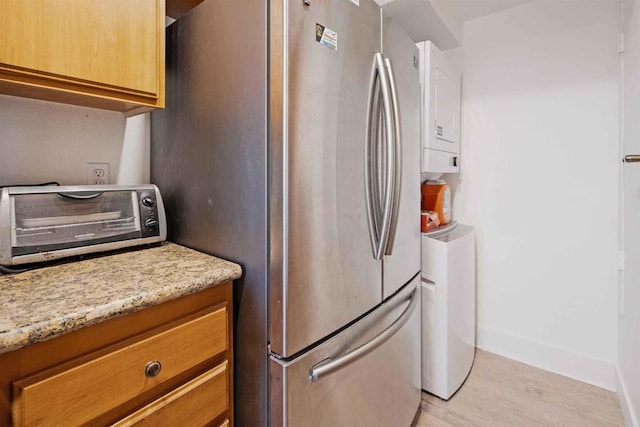 kitchen featuring light stone counters, freestanding refrigerator, a toaster, light wood-style floors, and baseboards
