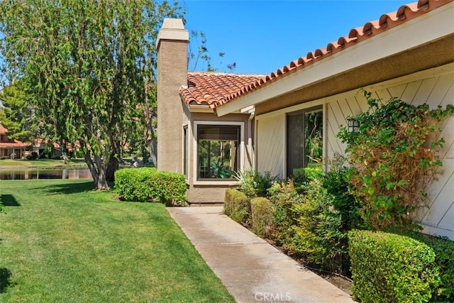 74 Tennis Club Dr, Rancho Mirage, CA 92270 - view of exterior entry with a tiled roof, a chimney, a lawn, a water view, and stucco siding