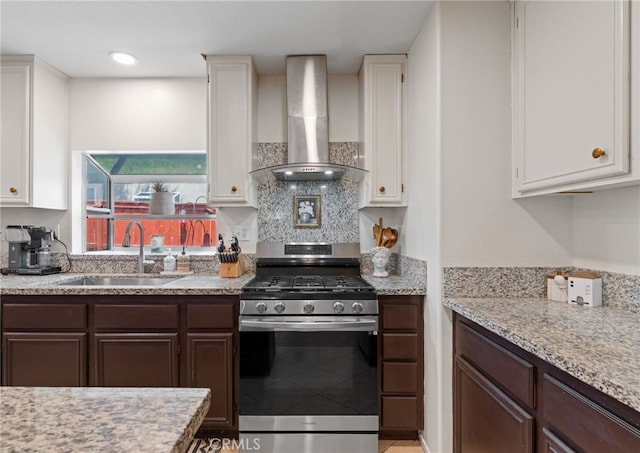 kitchen featuring a sink, wall chimney exhaust hood, gas stove, and white cabinetry